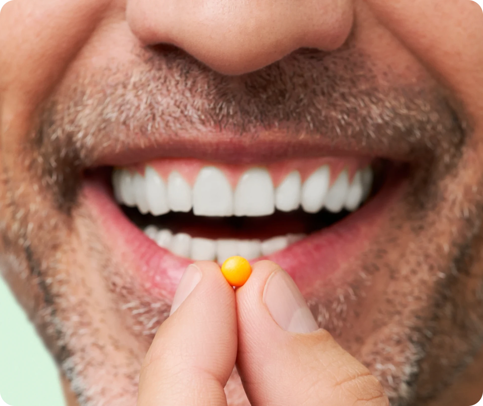 Man smiling while holding a small orange pill near his mouth.